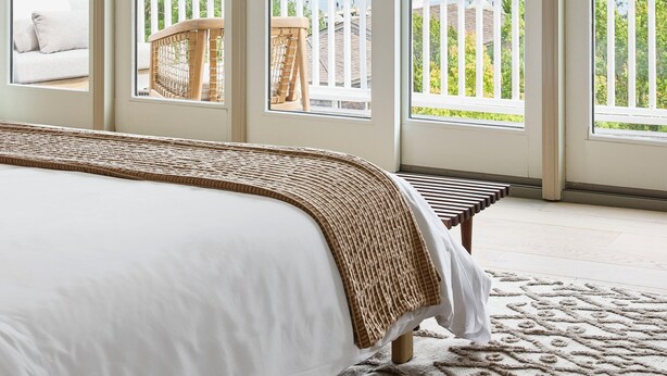 A bedroom with a large bed, a view of the outdoors through sliding glass doors, and a balcony with a white railing. - Faraway Martha's Vineyard (Edgartown)