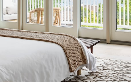 A bedroom with a large bed, a view of the outdoors through sliding glass doors, and a balcony with a white railing.