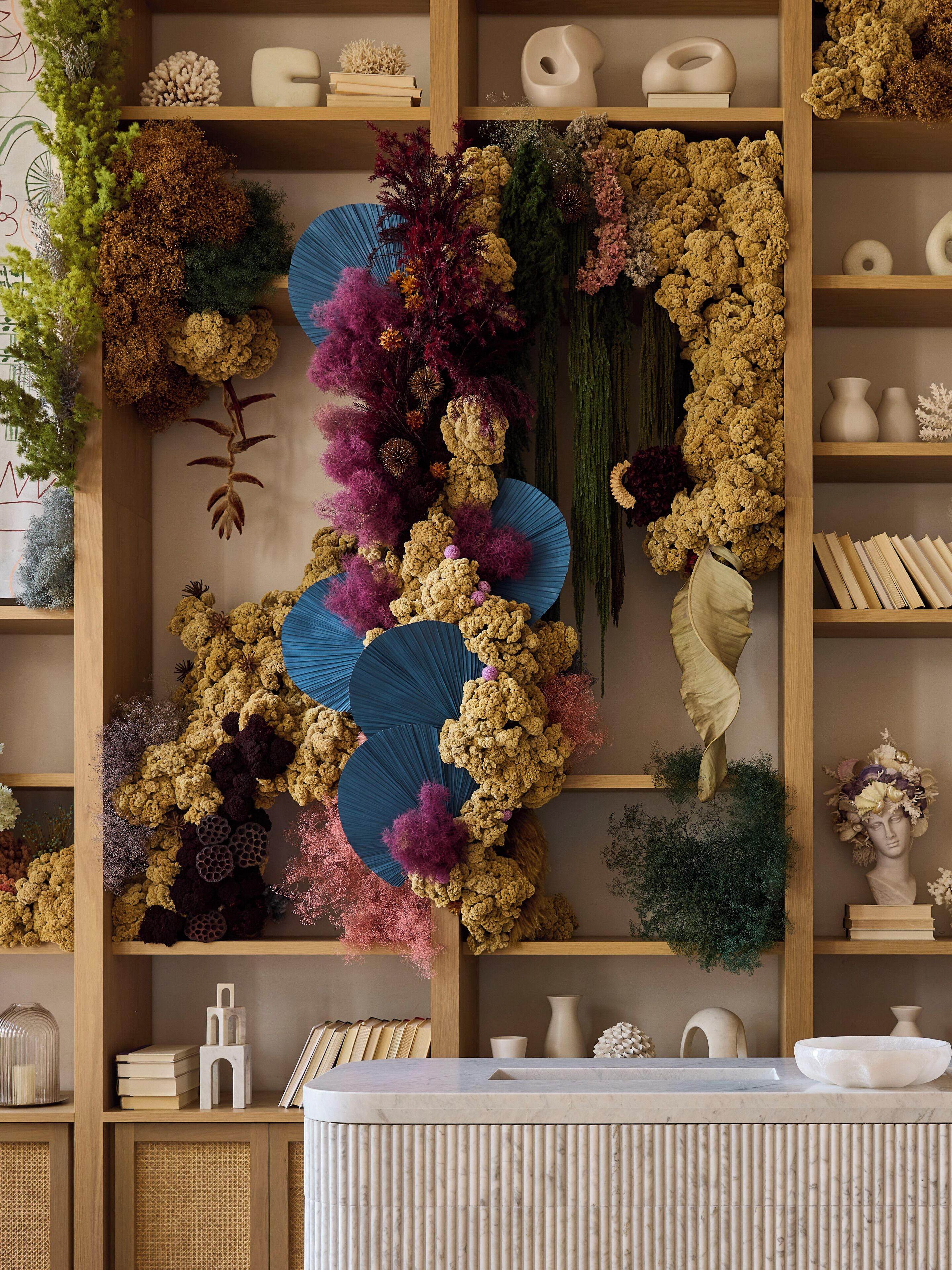 A room with a wooden bookshelf, a marble reception desk, and various decorative items including plants and vases.