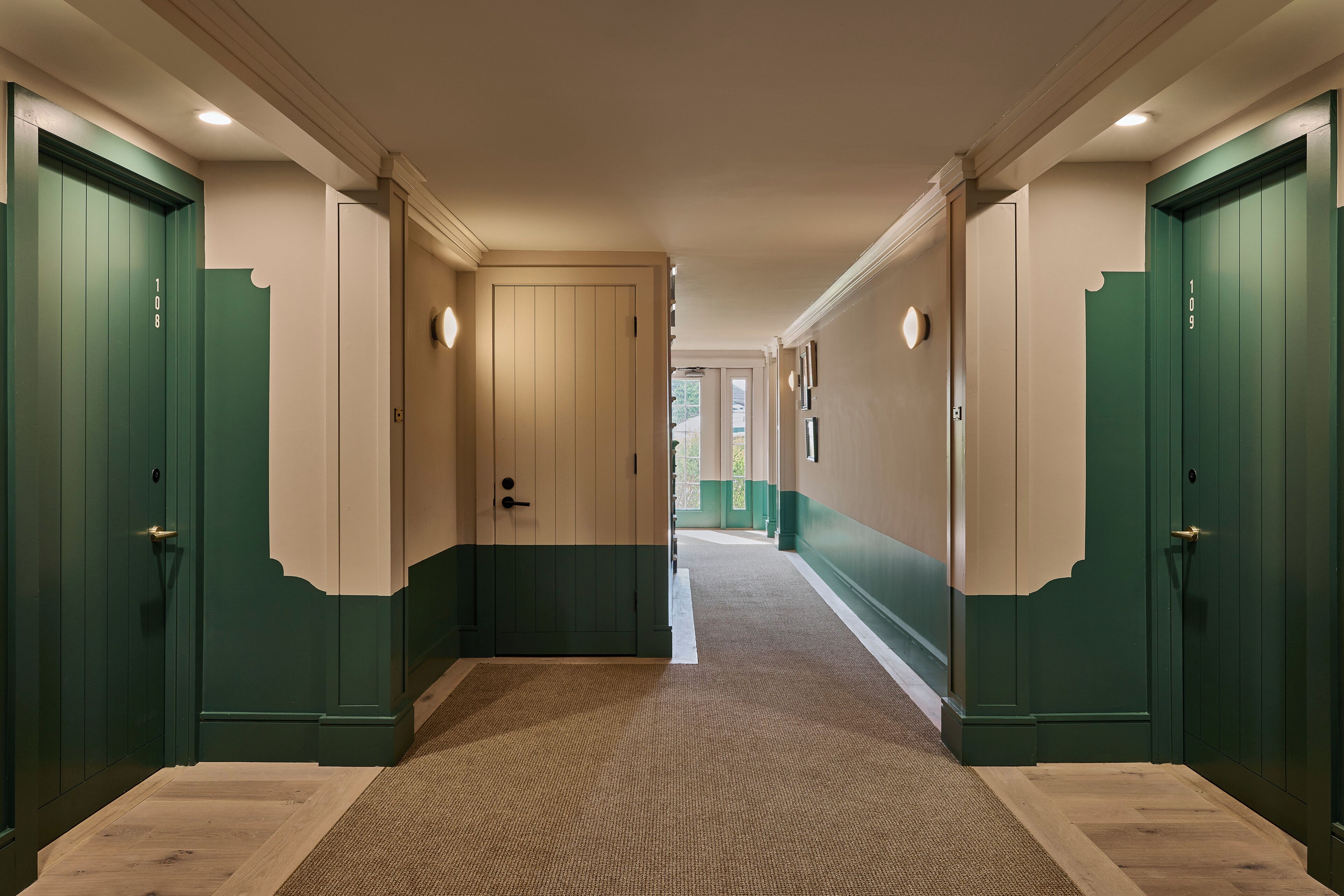 A hallway with green doors, beige walls, and a patterned carpet.