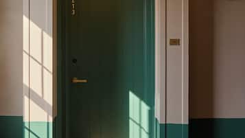 Une porte verte avec une poignée en laiton, une plaque de numéro et un luminaire fixé au mur.