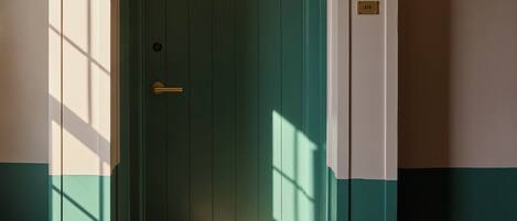A green door with a brass handle, a number plate, and a light fixture on the wall.