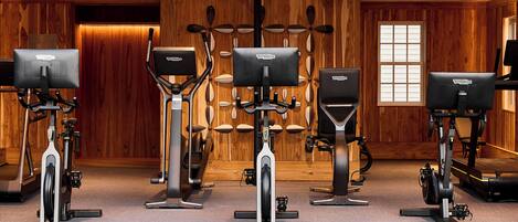 A row of stationary bikes with attached screens in a room with wooden paneling and a large window.