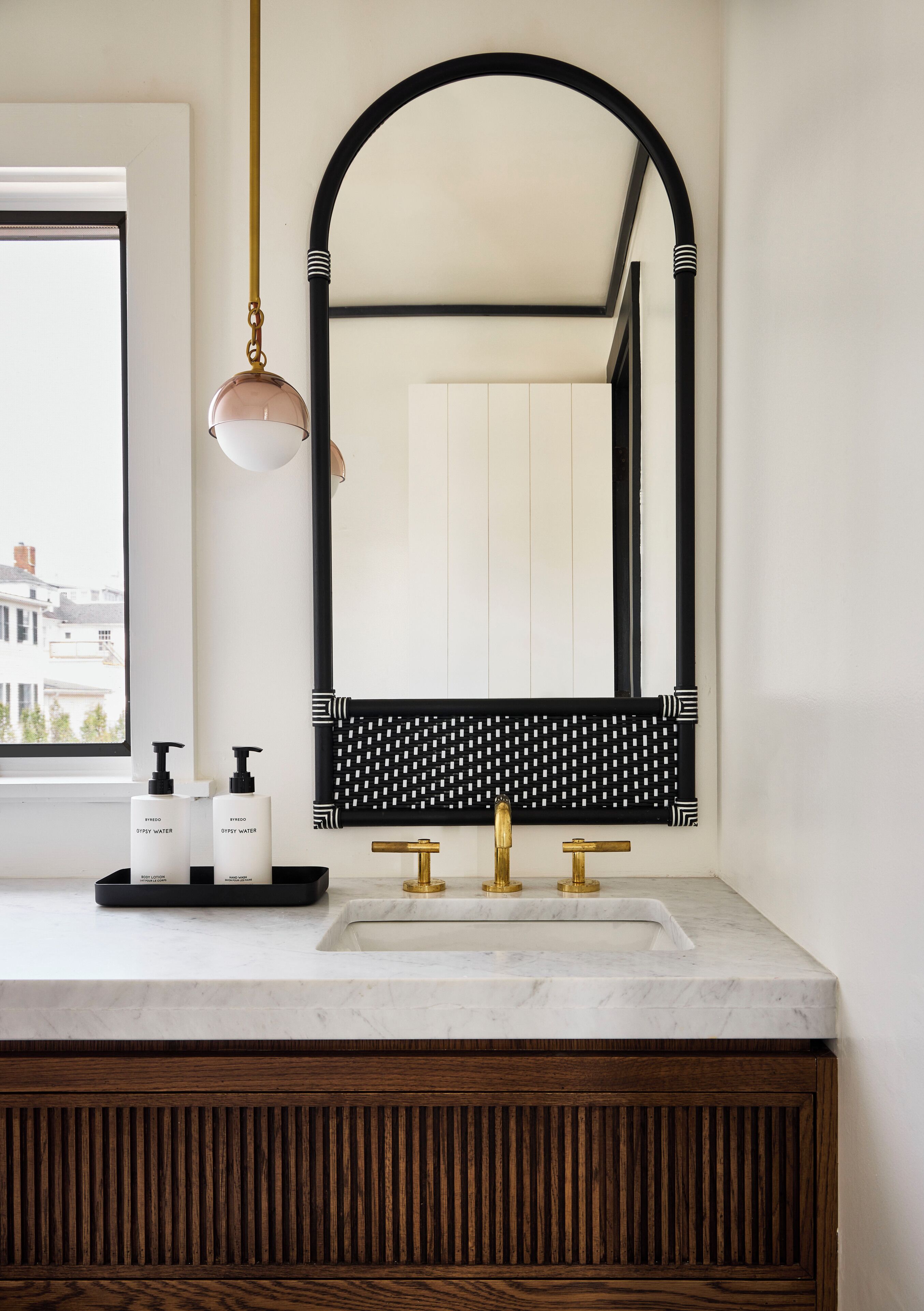 Une salle de bain avec un lavabo en marbre blanc, des robinetteries noires et dorées, et un grand miroir avec un cadre noir.
