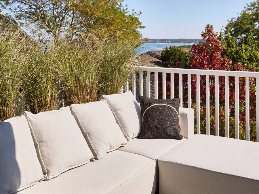 A white outdoor sofa with cushions, a white railing, and a view of the sea and trees.