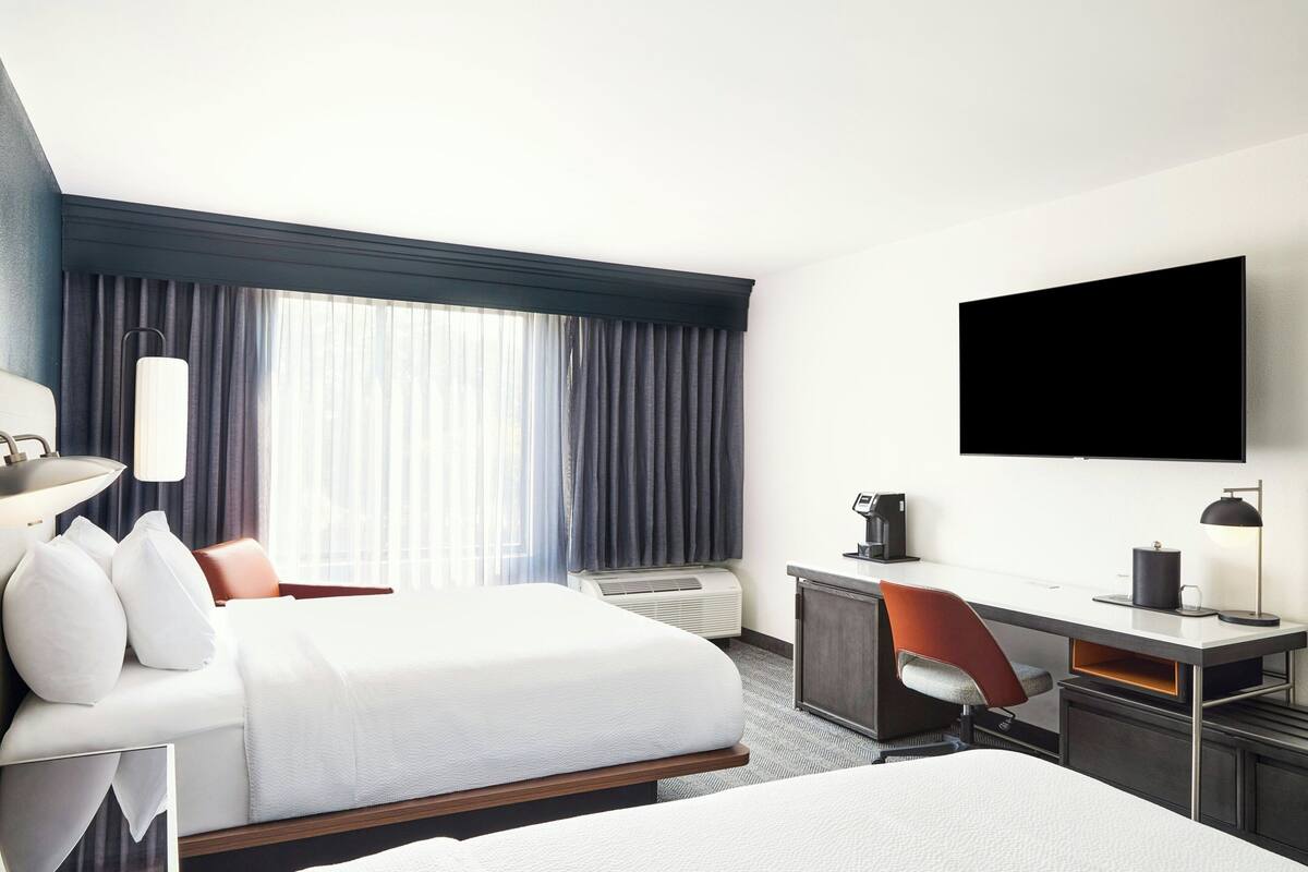 A hotel room with a bed, desk, chair, TV, and air conditioning unit.