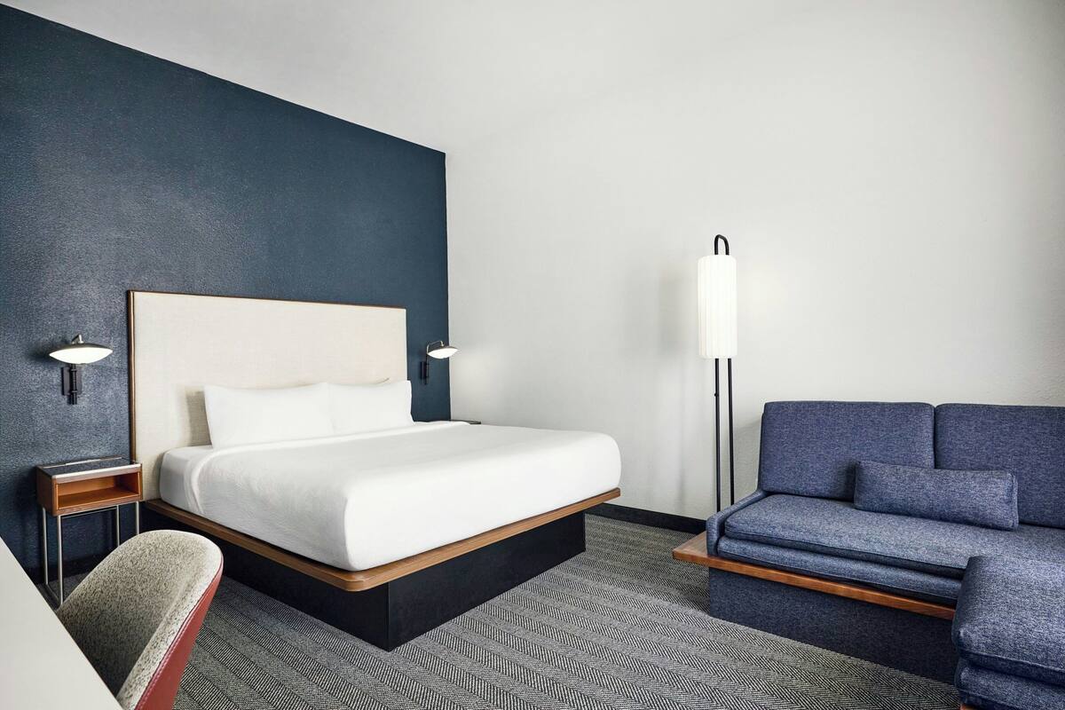 A hotel room with a bed, a sofa, a nightstand, and a lamp.