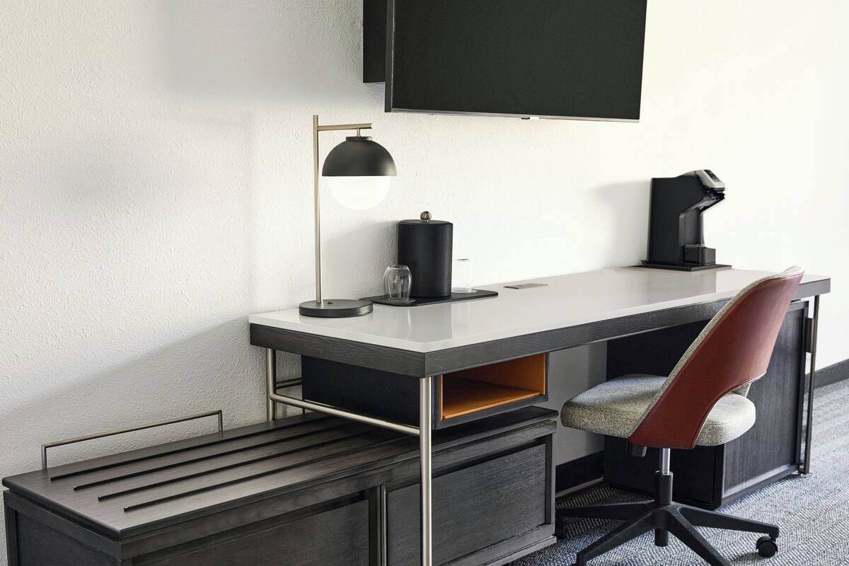 A modern office desk with a flat-screen TV, a desk lamp, a coffee maker, and a chair.