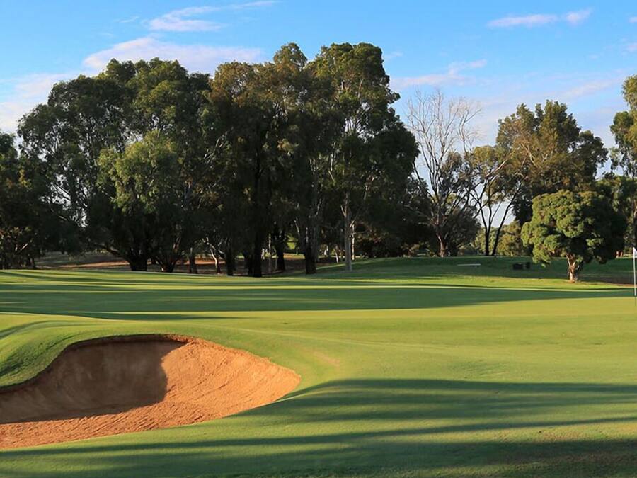 A golf course with a sand bunker, trees, and a clear sky.