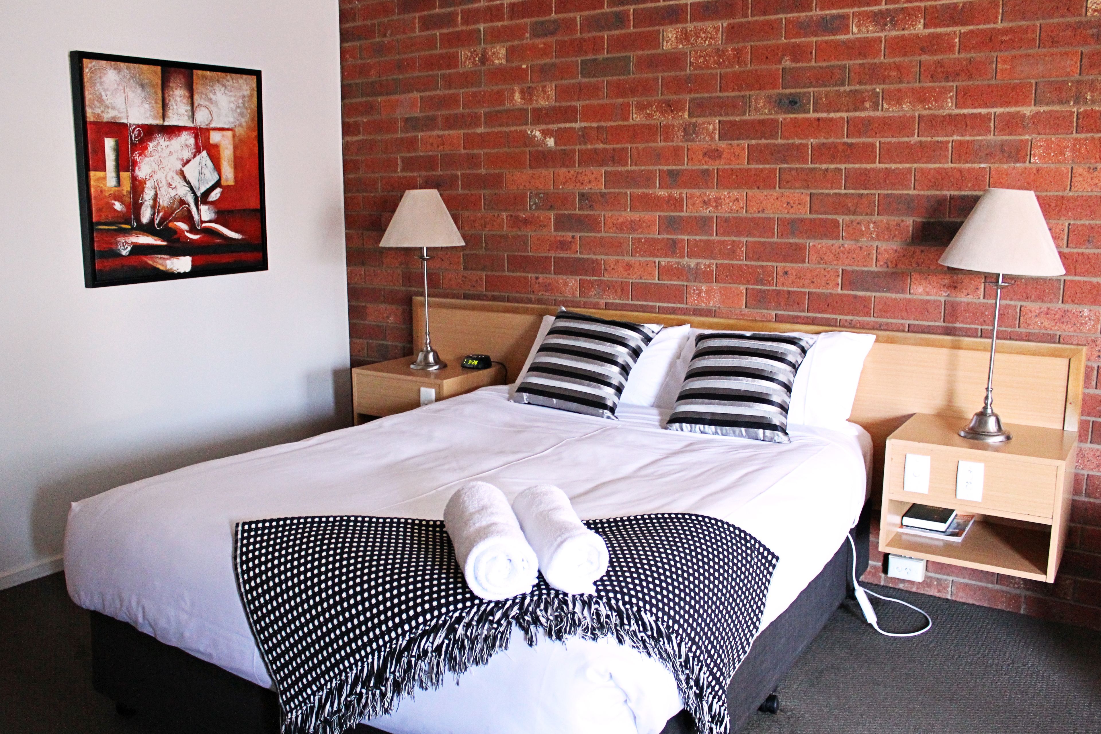 Een hotelkamer met een groot bed, twee nachtkastjes, een bakstenen muur en een schilderij aan de wand.