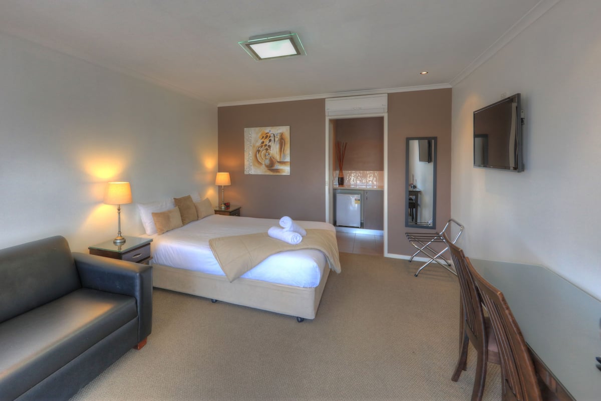 A hotel room with a bed, a sofa, a desk with a lamp, a TV, and a mirror.
