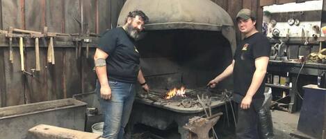 Two individuals working with a large, industrial forge in a workshop setting.