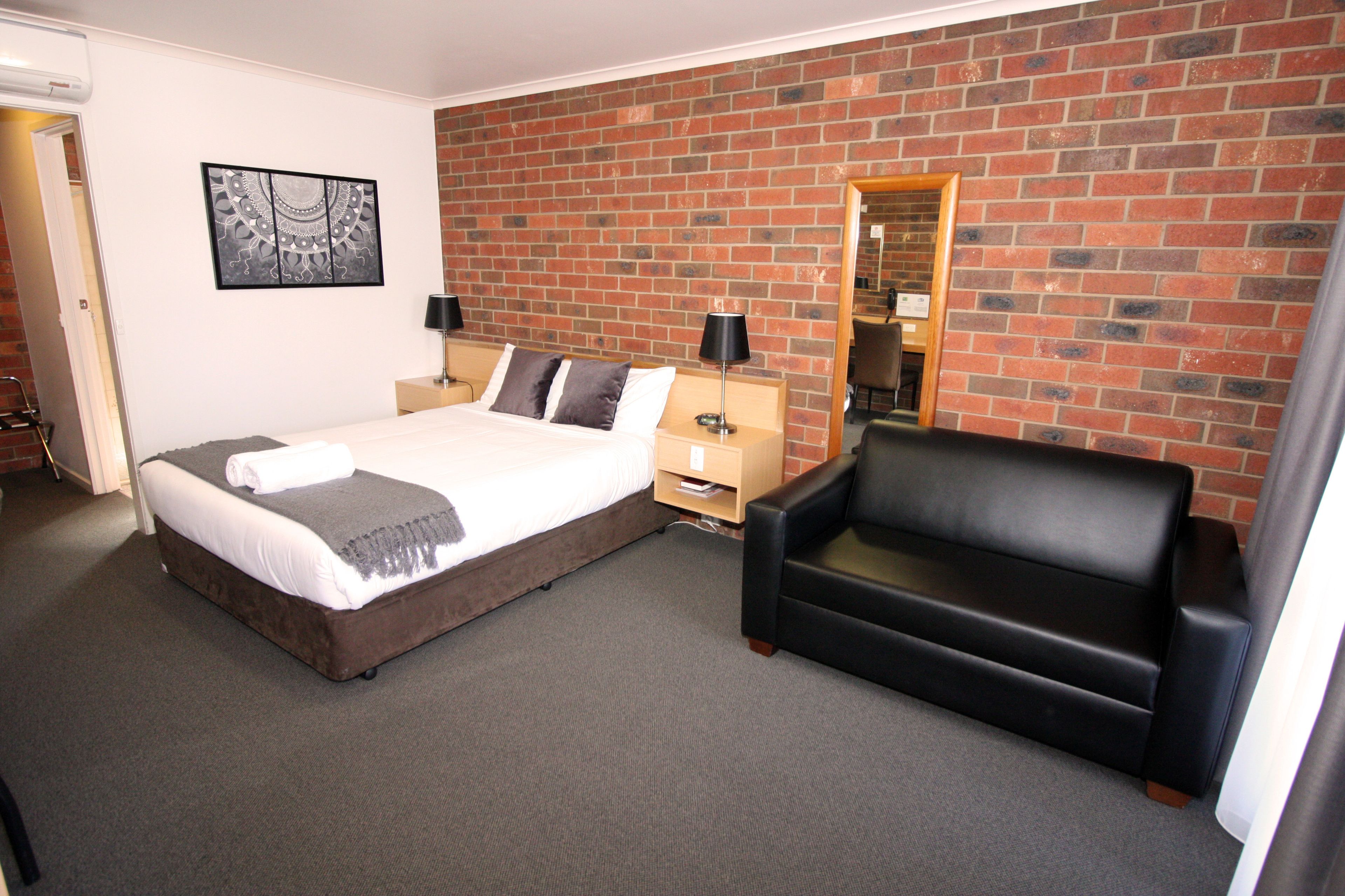 Ein Hotelzimmer mit einem großen Bett, einer schwarzen Leder-Couch, einer Ziegelwand und einem Spiegel.