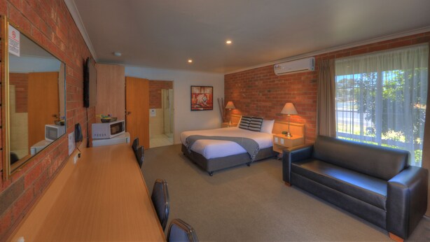 Habitación de hotel con cama, sofá, escritorio, microondas y un ventanal grande.