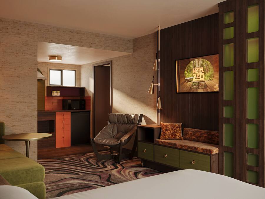 Ett modernt hotellrum med en säng, en grön soffa, en stol, ett skrivbord och en liten köksdel.