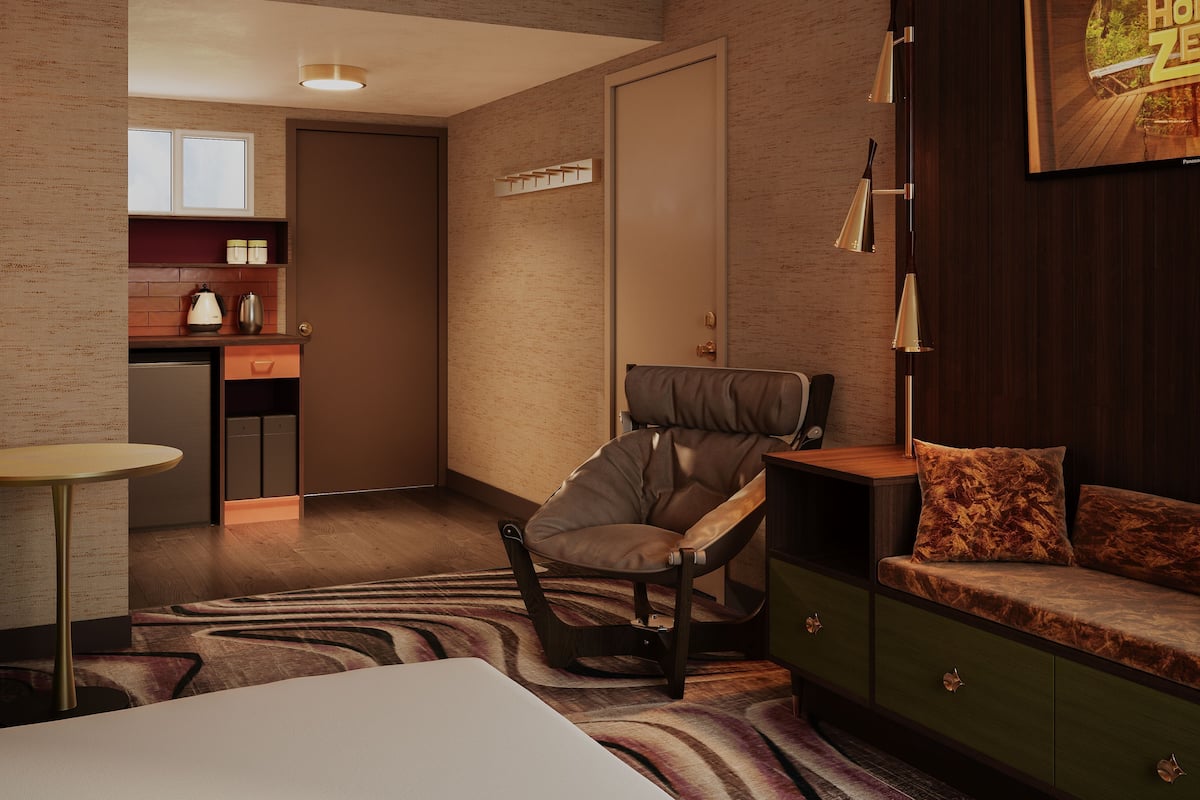 A modern hotel room with a bed, a sofa, a desk, and a kitchenette.