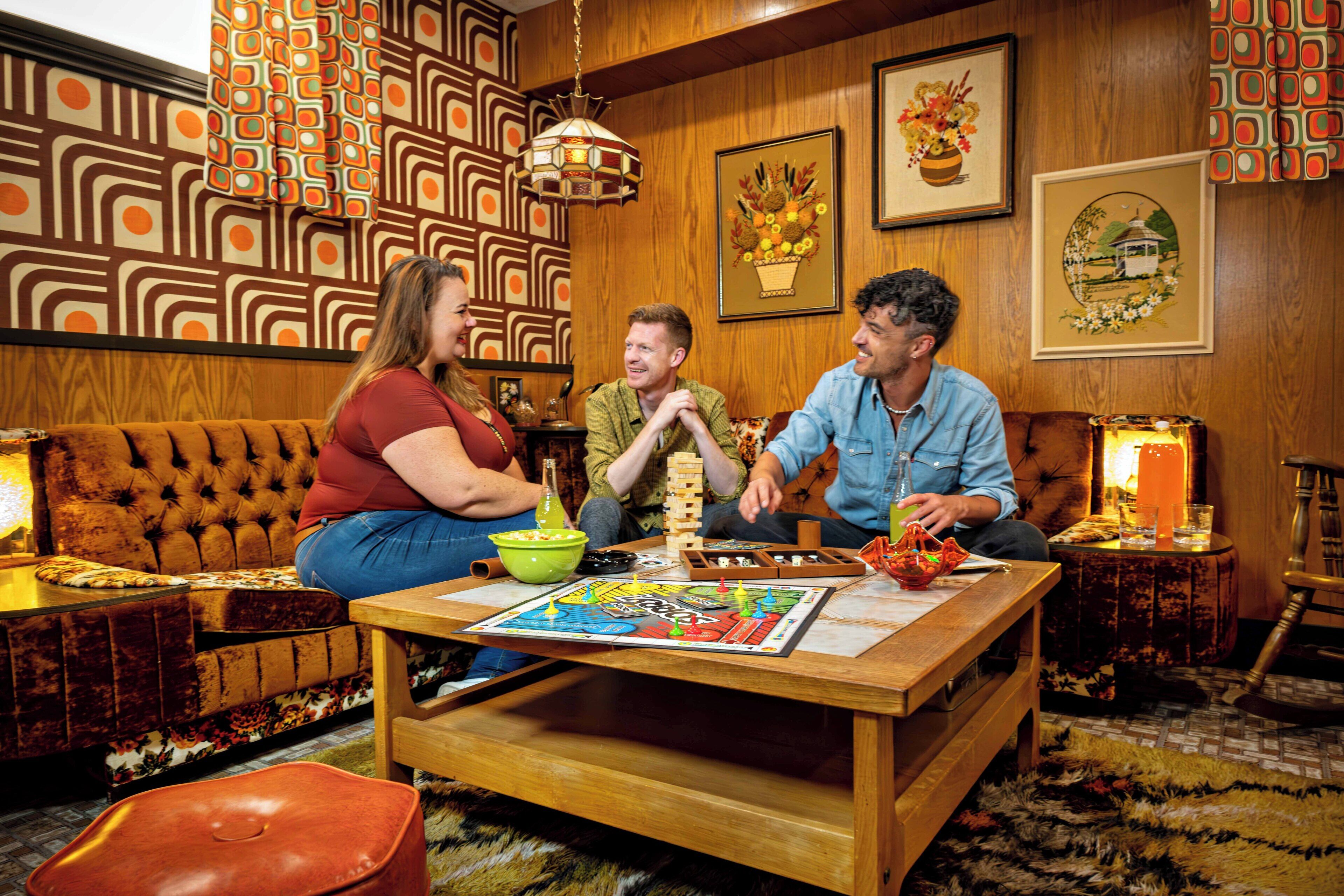 A cozy room with a patterned wall, a wooden table with a board game, a sofa, and a lamp.
