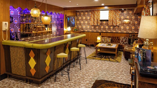 Zona de bar con taburetes, pared con diseño y área de estar con alfombra.