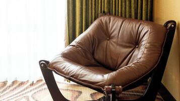 A brown leather chair with a black metal frame, positioned on a patterned carpet, next to a window with sheer curtains.