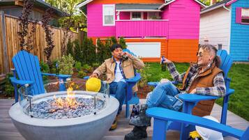A patio with a fire pit, blue Adirondack chairs, and a small table.