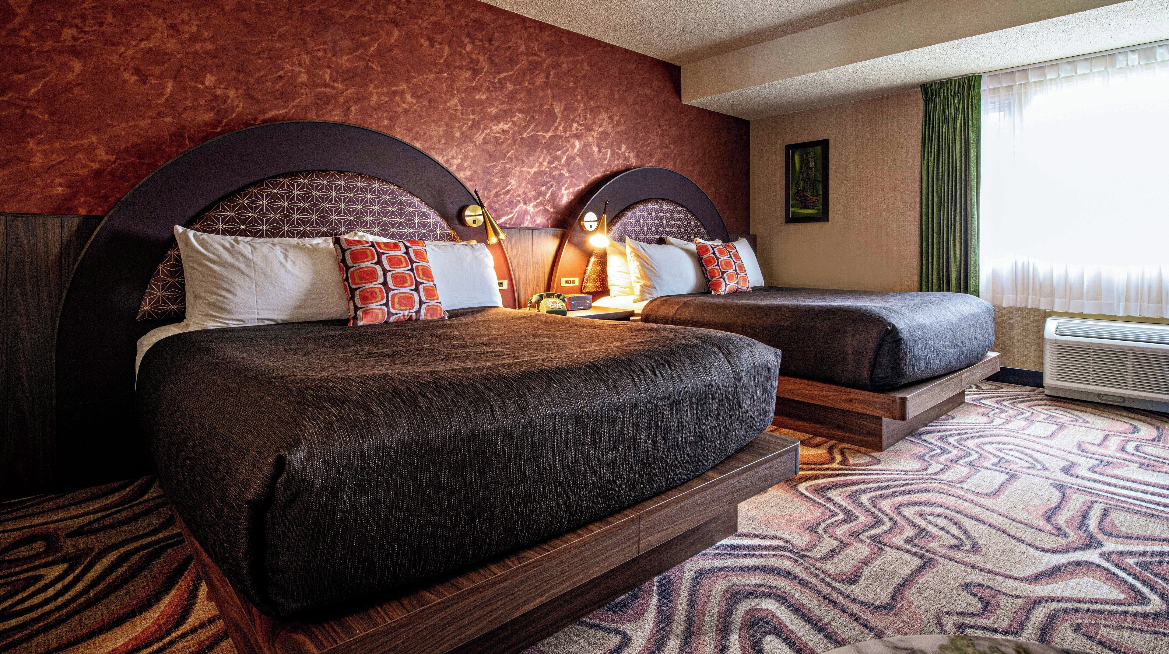 Una camera d'albergo con due letti, una moquette fantasia e un'ampia finestra con tende.