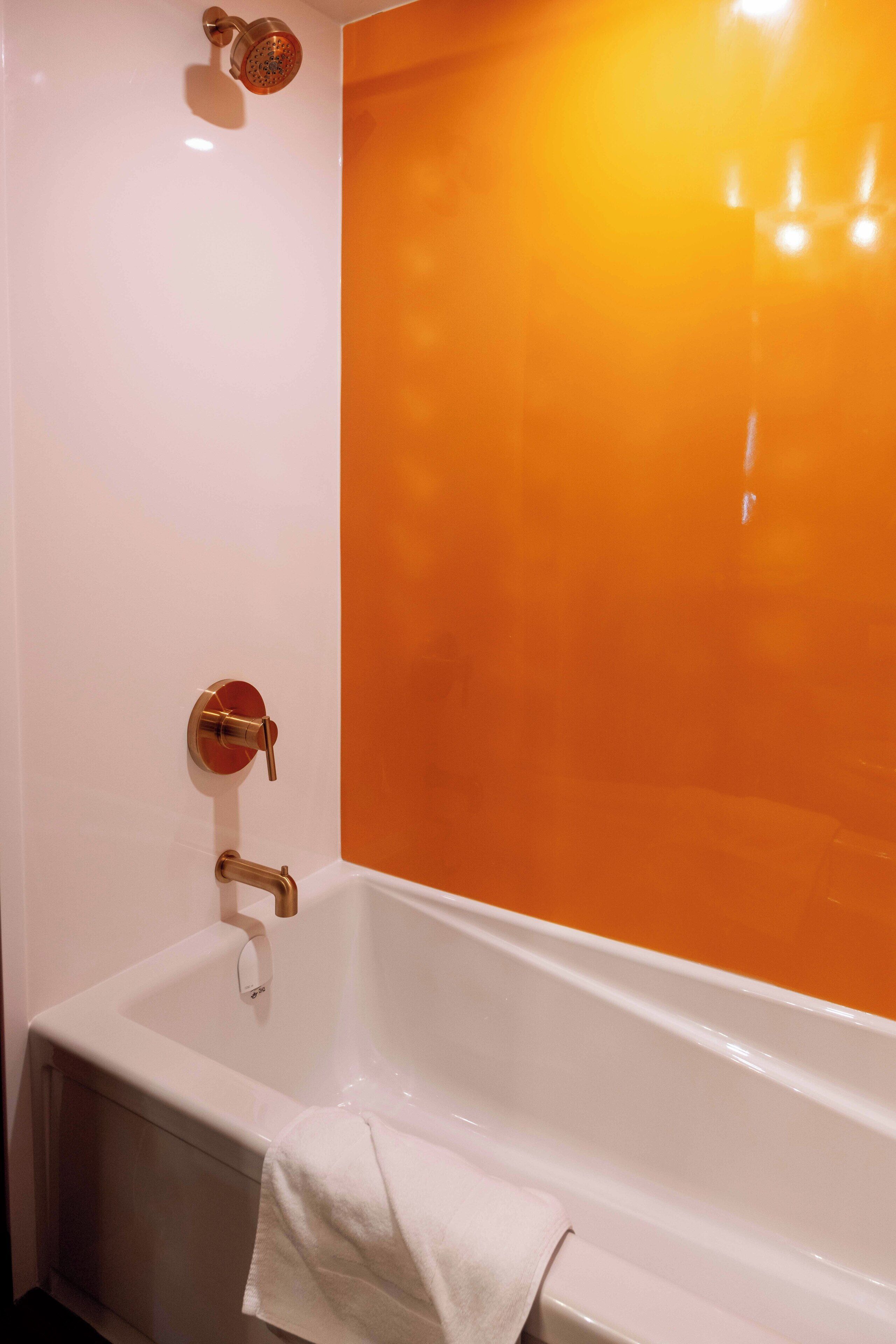 A bathroom with a white bathtub, a gold showerhead, and an orange-tinted wall.