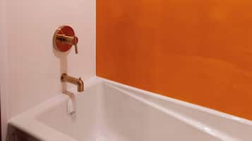 A bathroom with a white bathtub, a gold showerhead, and an orange-tinted wall.