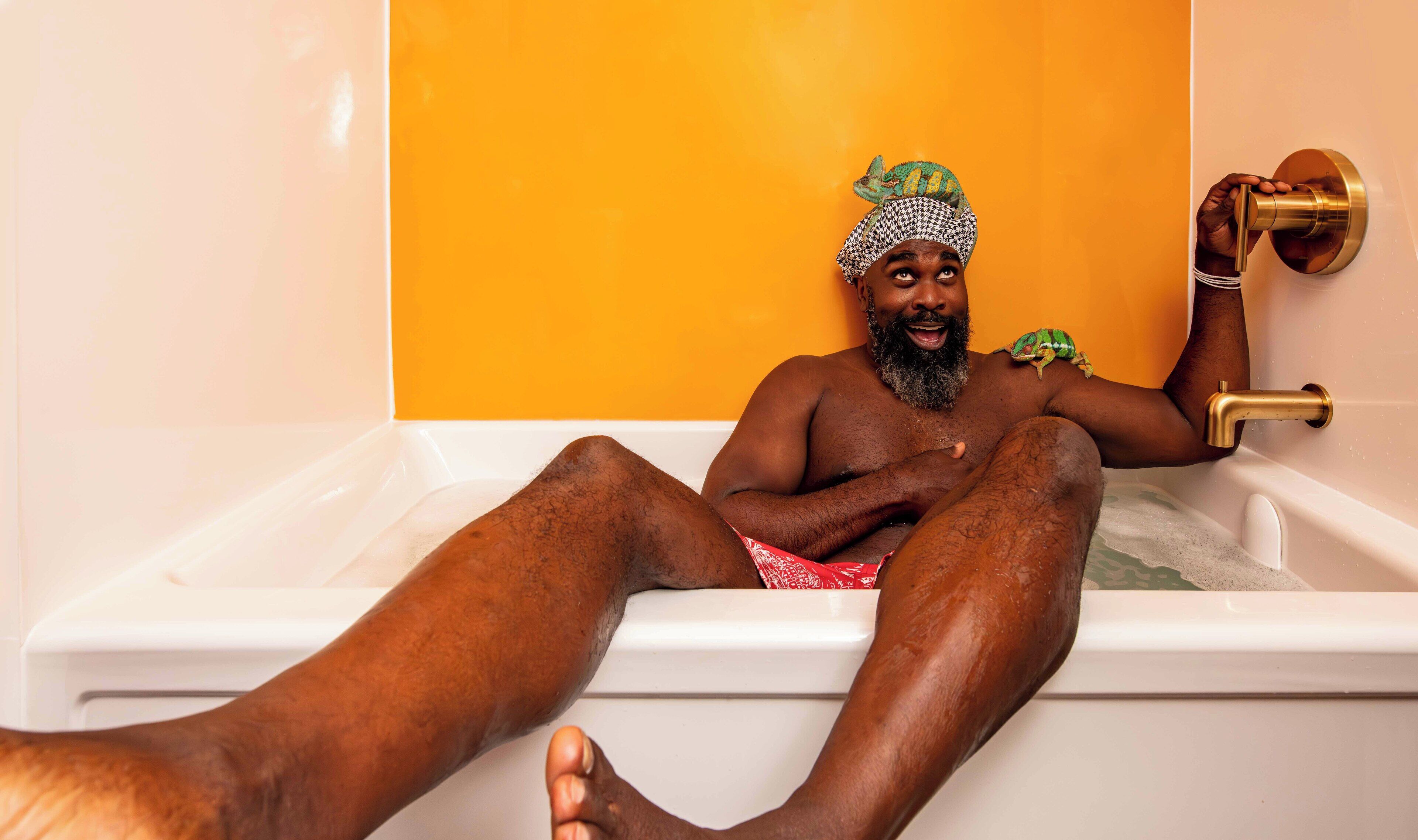 A person sitting in a bathtub with a green frog on their shoulder, a gold faucet, and a white bathtub.