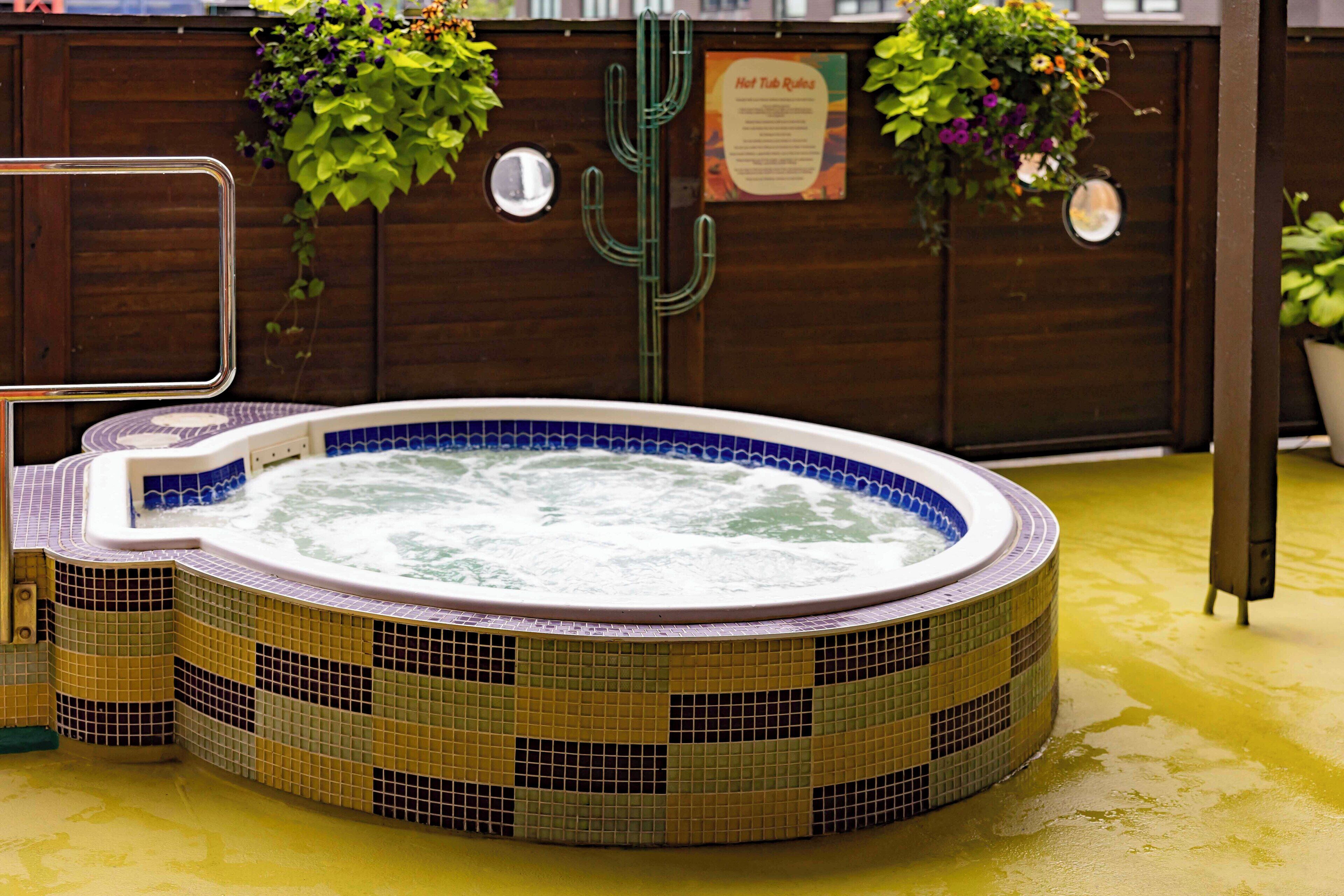 Un bain à remous dont les parois sont recouvertes de mosaïques, entouré de panneaux en bois et agrémenté de plantes en pot.