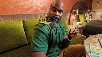 A man sitting on a green sofa with a frog on his shoulder, holding a card.