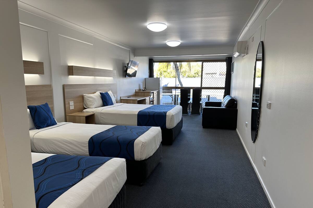 A hotel room with two beds, a desk, a chair, a TV, and a large window.
