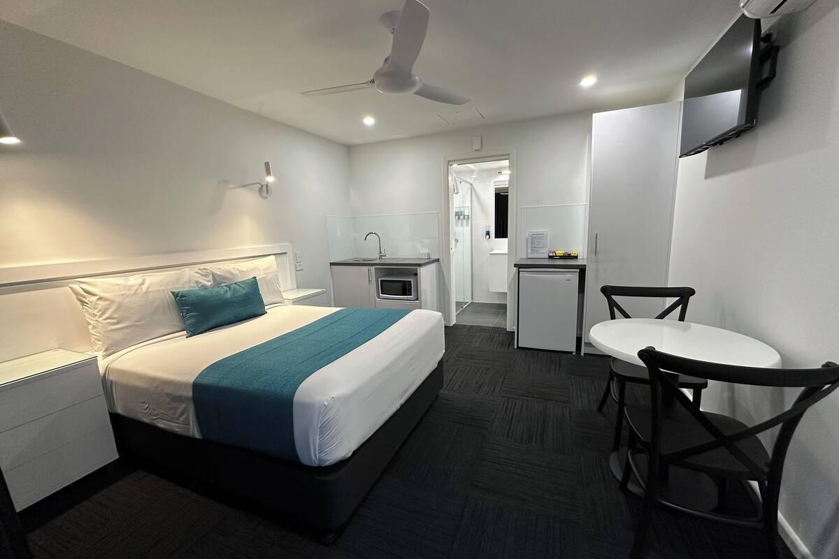 A hotel room with a bed, a desk, a chair, a microwave, and a ceiling fan.