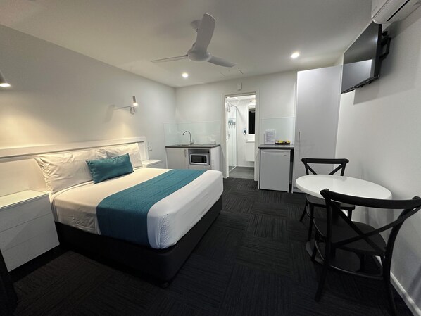 A hotel room with a bed, a desk, a chair, a microwave, and a ceiling fan.