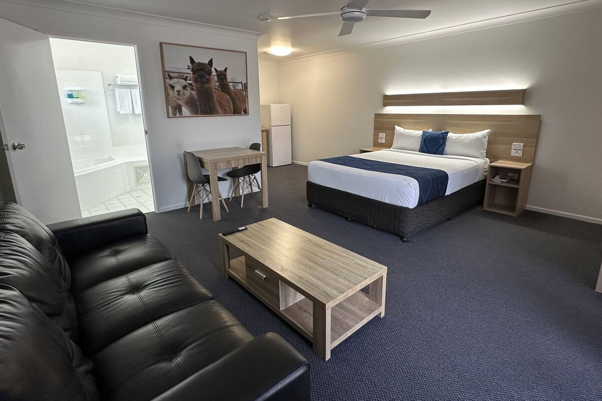 A modern hotel room with a bed, a desk, a chair, a sofa, and a ceiling fan.
