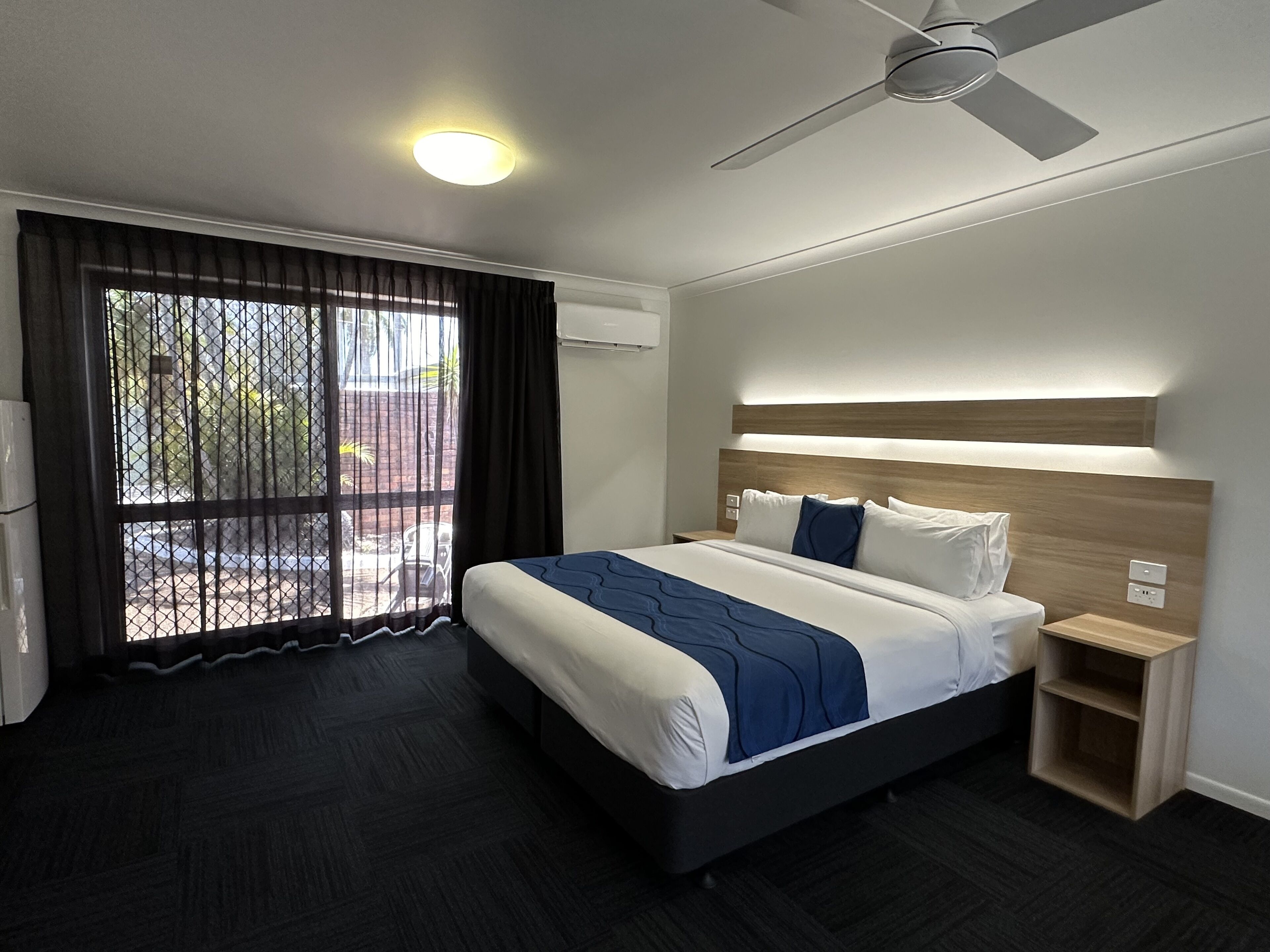 Habitación de hotel moderna con una cama grande, un ventilador de techo y vistas al exterior a través de una puerta corrediza.