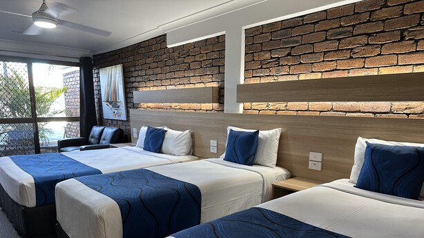 A hotel room with three beds, a brick wall, and a large window.