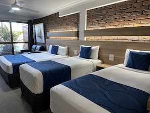 A hotel room with three beds, a brick wall, and a large window.