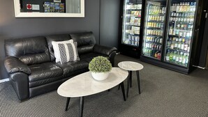 A modern lounge area with a black leather sofa, a small round table with a potted plant, and a refrigerator stocked with beverages.