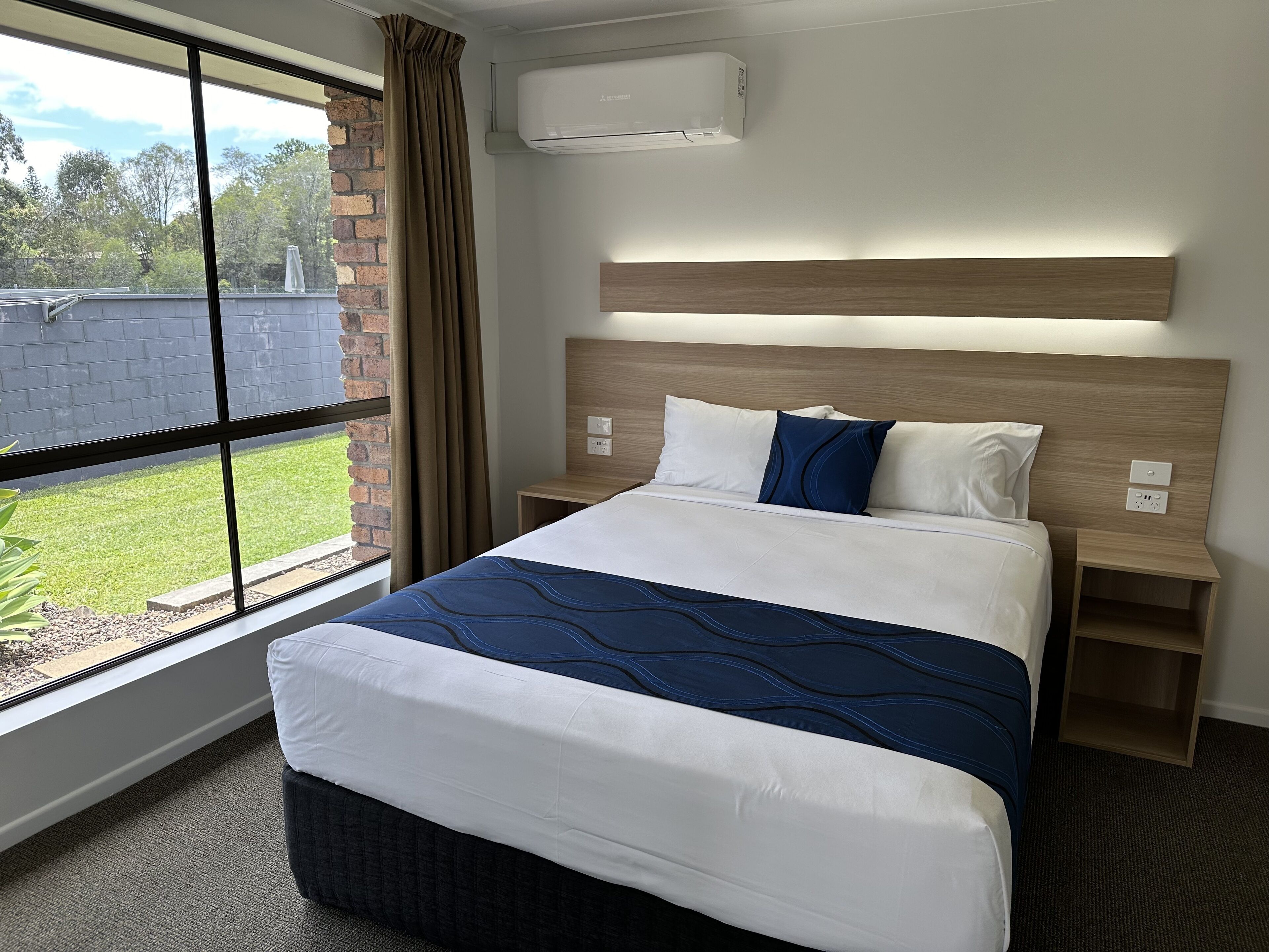 A hotel room with a large bed, a headboard, a nightstand, and a window with curtains.