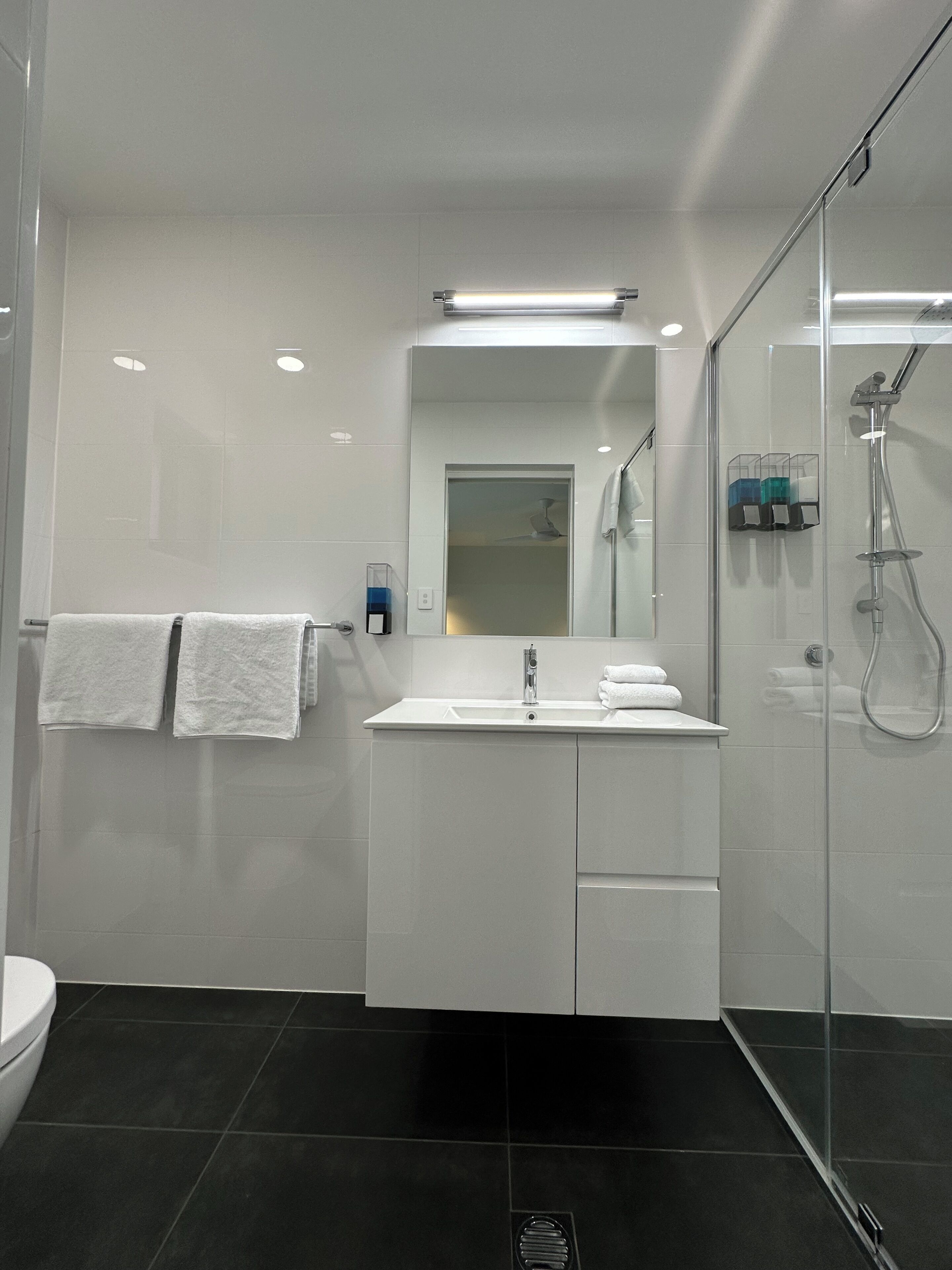 A modern bathroom with a glass shower enclosure, a white vanity with a mirror, and two towels hanging on the wall.