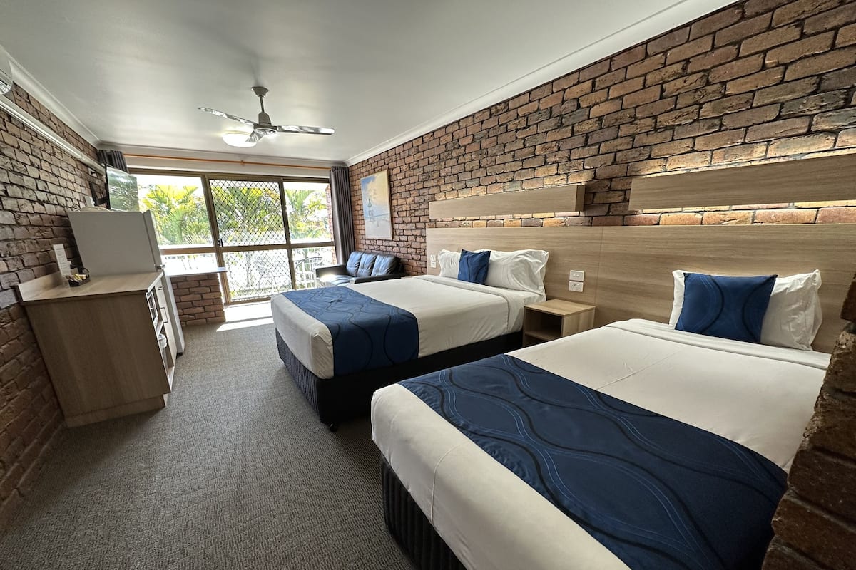 A hotel room with two beds, a desk, and a window with a view of greenery.