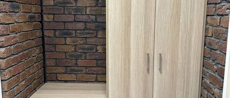 A room with a brick wall, a wooden bench, and a wardrobe with two doors.