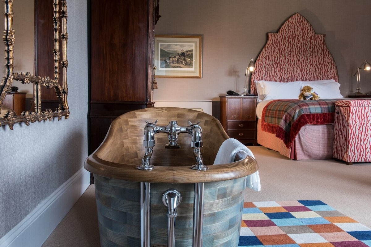 A bathroom with a wooden bathtub, a mirror, and a bed with a patterned headboard.