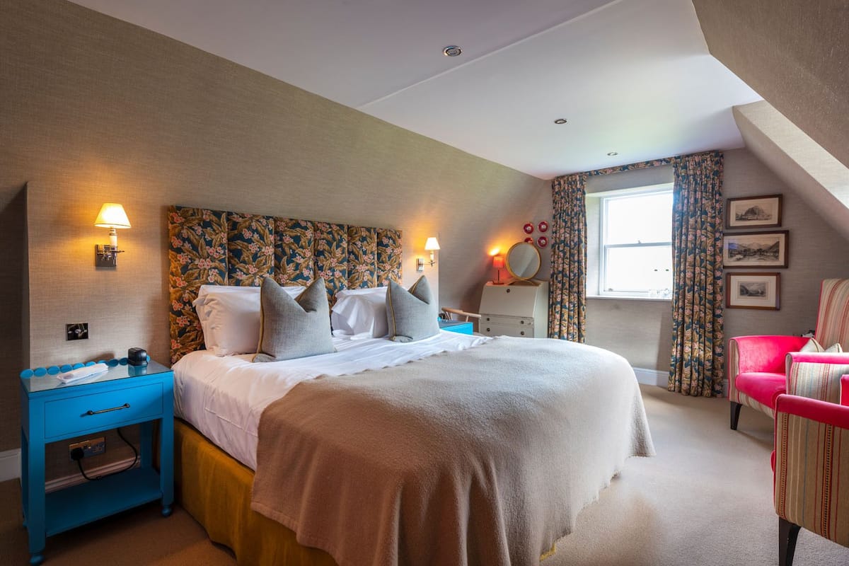 A bedroom with a large bed, a nightstand, a dresser, a chair, and a window with curtains.
