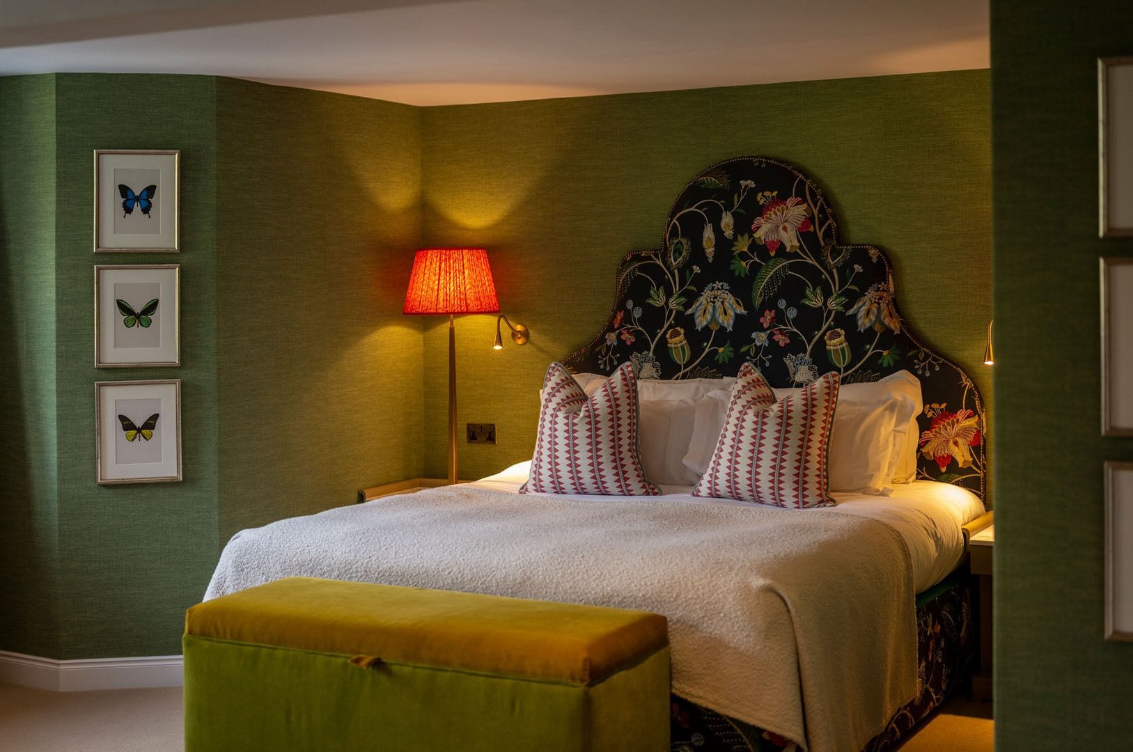 A neatly made bed with patterned pillows, a bedside lamp, and framed butterfly art on the wall.