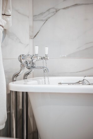 A modern bathroom with a freestanding bathtub, chrome fixtures, and marble walls.