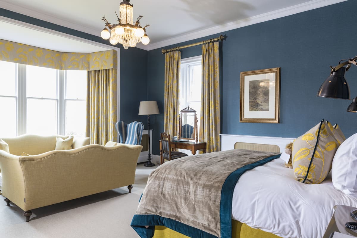 A bedroom with a bed, a sofa, a chair, a lamp, a mirror, and a chandelier.