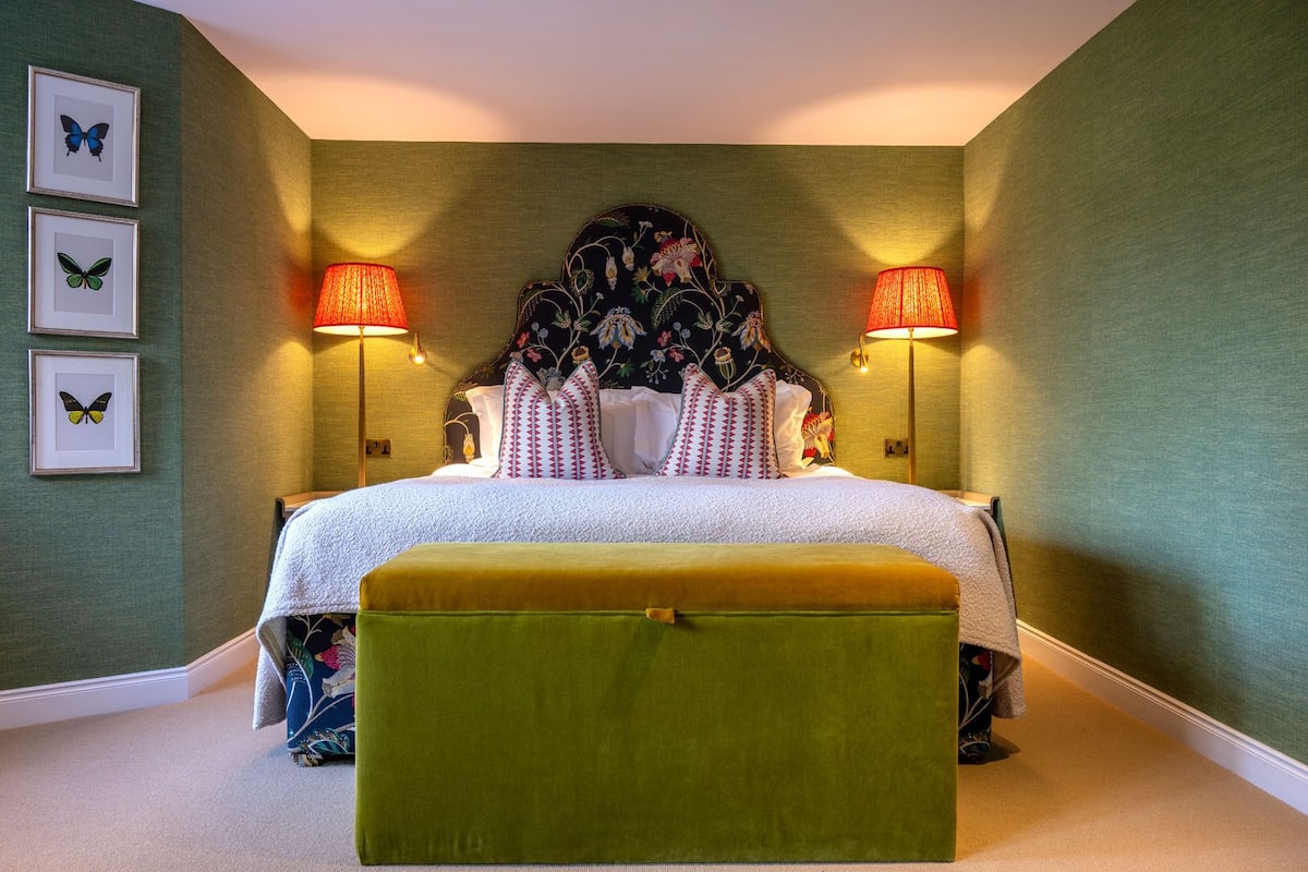 A neatly arranged bedroom with a bed, two bedside lamps, a headboard with floral patterns, and three framed butterfly pictures on the wall.