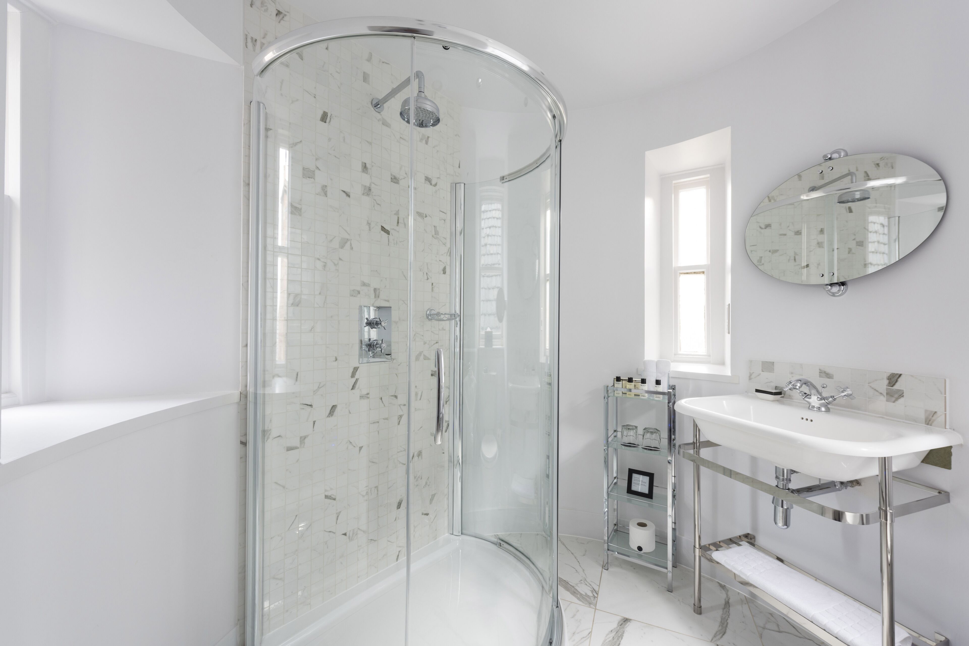 A modern bathroom with a glass-enclosed shower, a white sink with chrome fixtures, and a marble-tiled floor.