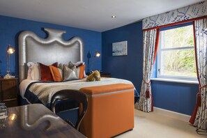 A bedroom with a large bed, a wooden nightstand, a desk, and a window with curtains.